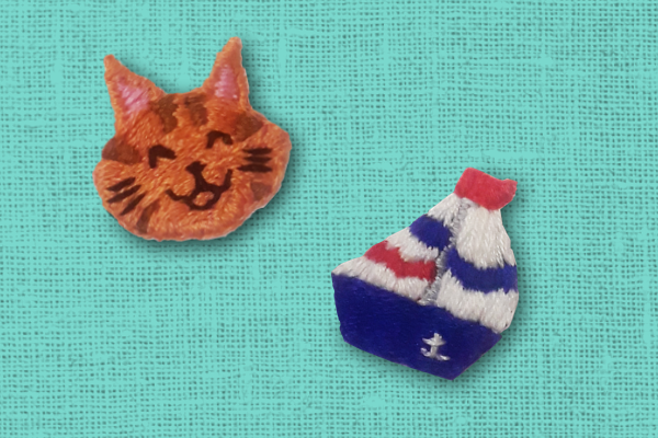 Simple hand-embroidered patch of a tabby cat face and a blue sailboat